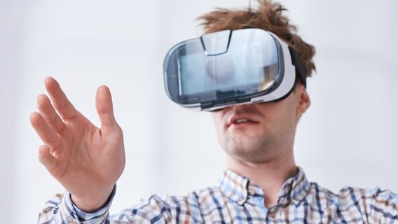 Mann trägt eine VR-Brille und fühlt mit seiner rechten Hand in den Raum. © fotolia.com Foto: Photographee.eu