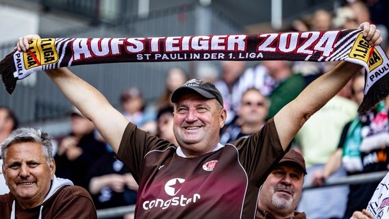 Ein Fan des FC St. Pauli hält einen Schal mit der Aufschrift "Aufsteiger 2024" in die Höhe. © picture alliance/dpa | Axel Heimken 